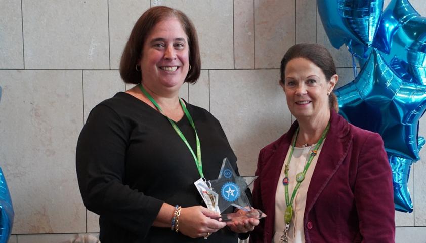 Two women standing together with one holding an award in her hand and smiling