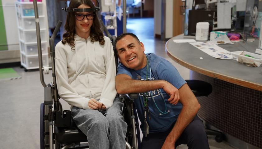 Teen in a wheelchair and her clinician sitting next to her smiles 
