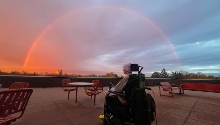 A young boy who uses a wheelchair looks up at a rainbow in the sky