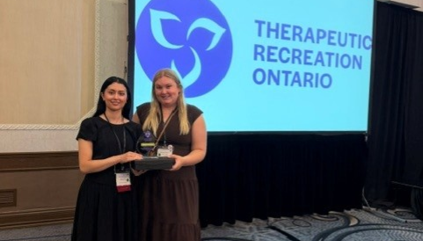 Two female therapeutic recreation specialists standing in a room holding an award