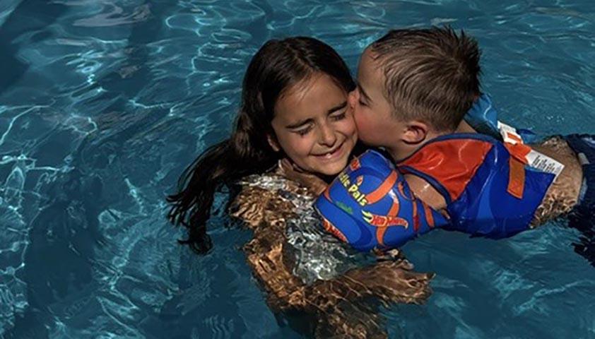 A boy is giving a kiss to an older girl, both of them are swimming