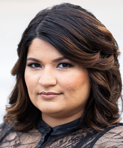 Dark-haired woman looking at the camera wearing a black lace shirt.