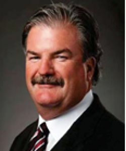 Man with brown hair and a moustache wearing a black blazer and striped tie