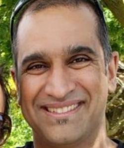 Man with buzzed brown hair and goatee smiling with sunglasses on top of his head