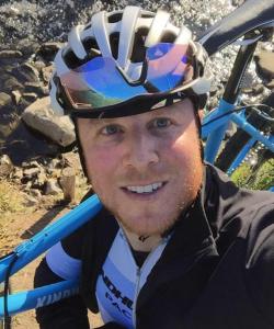Man wearing a biking helmet while holding a blue bicycle on his shoulder