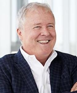 Man with white hair wearing a blue plaid blazer and a white shirt.