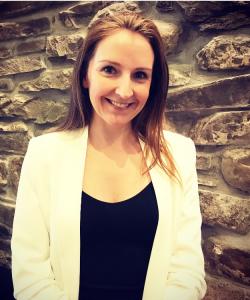 Woman with long dark hair in a black shirt and white blazer