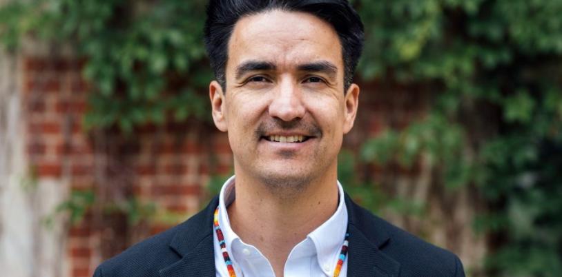 Man with dark hair and colourful necklace