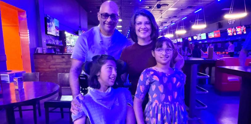 Girl in wheelchair with another girl beside her and man and woman behind in bowling alley