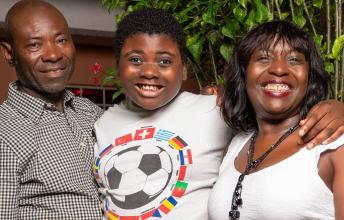 Teen wearing soccer shirt smiles with arms around another man and woman