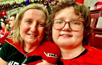 Woman with blonde hair and red cape with younger woman with brown hair, glasses and red cape in stands holding a Raptors mascot doll