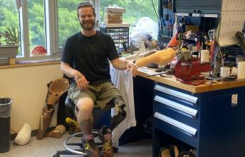 Man with beard and prosthetic leg sits on chair beside work table with tools