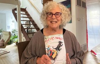 Woman with wavy white hair holds children's book