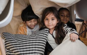 A girl and two boys play behind pillows