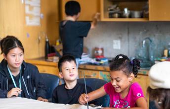 A teenager is teaching two children to draw