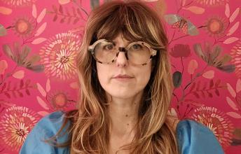 Woman with long hair and glasses against a pink wallpaper