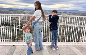 An older sister and her two younger brothers stand on a balcony.