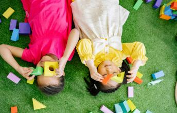 Young girls lie on floor playing with blocks