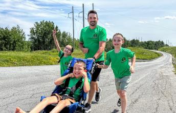 A dad and three children run together outdoors using an adapted stroller