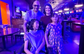 Girl in wheelchair with another girl beside her and man and woman behind in bowling alley