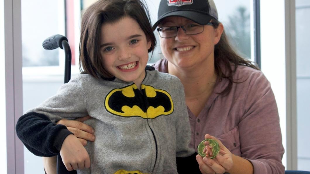 Girl wearing batman shirt in wheelchair with mom holding a clay art piece