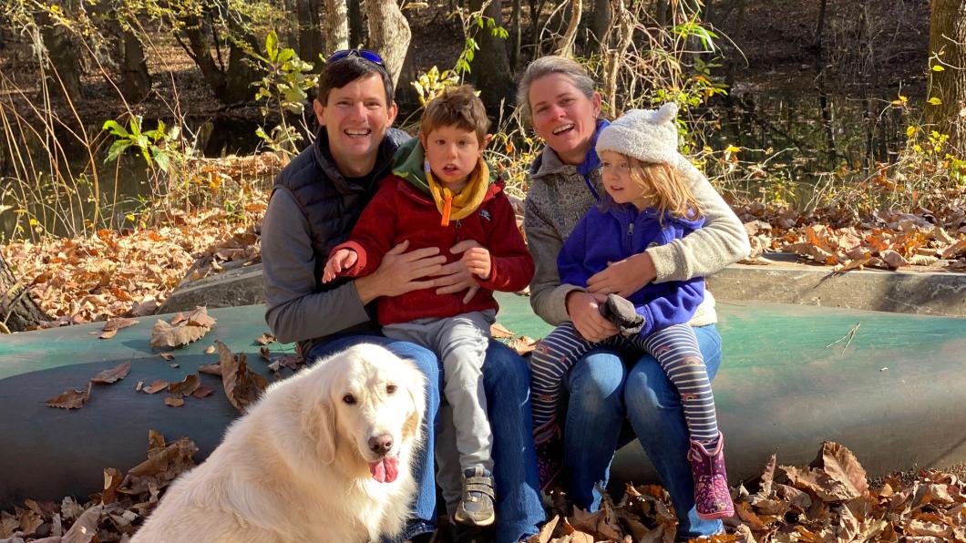 Mother and father sitting on upturned canoe with two young children and dog