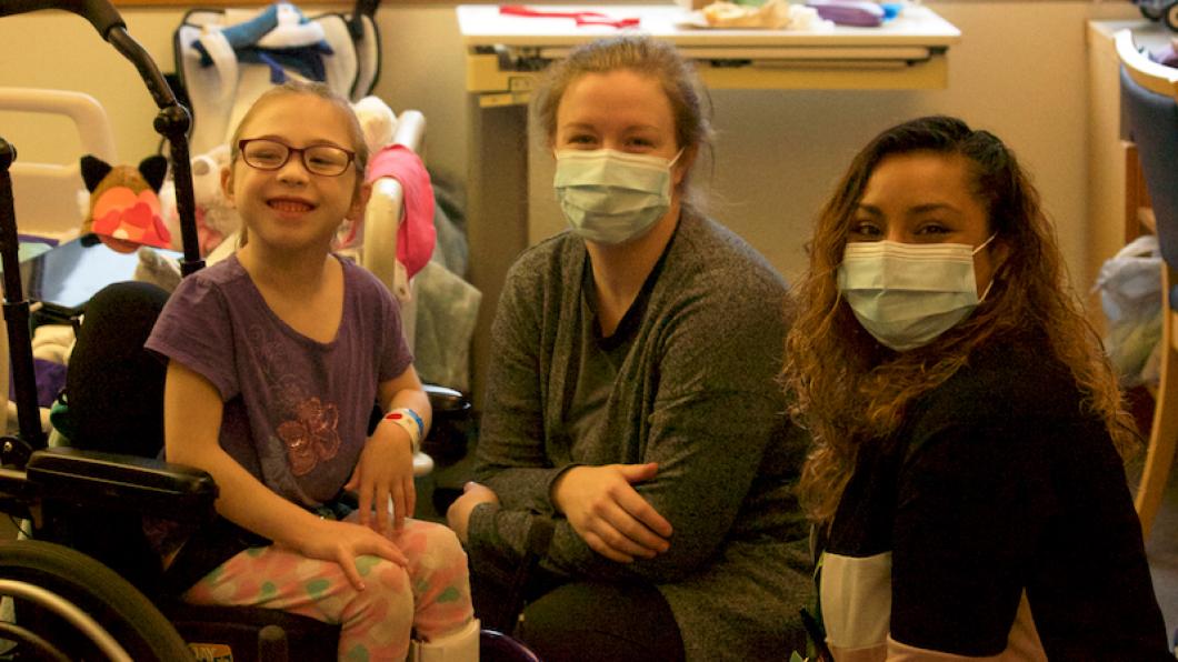 Girl in wheelchair with mother and nurse in masks smiling