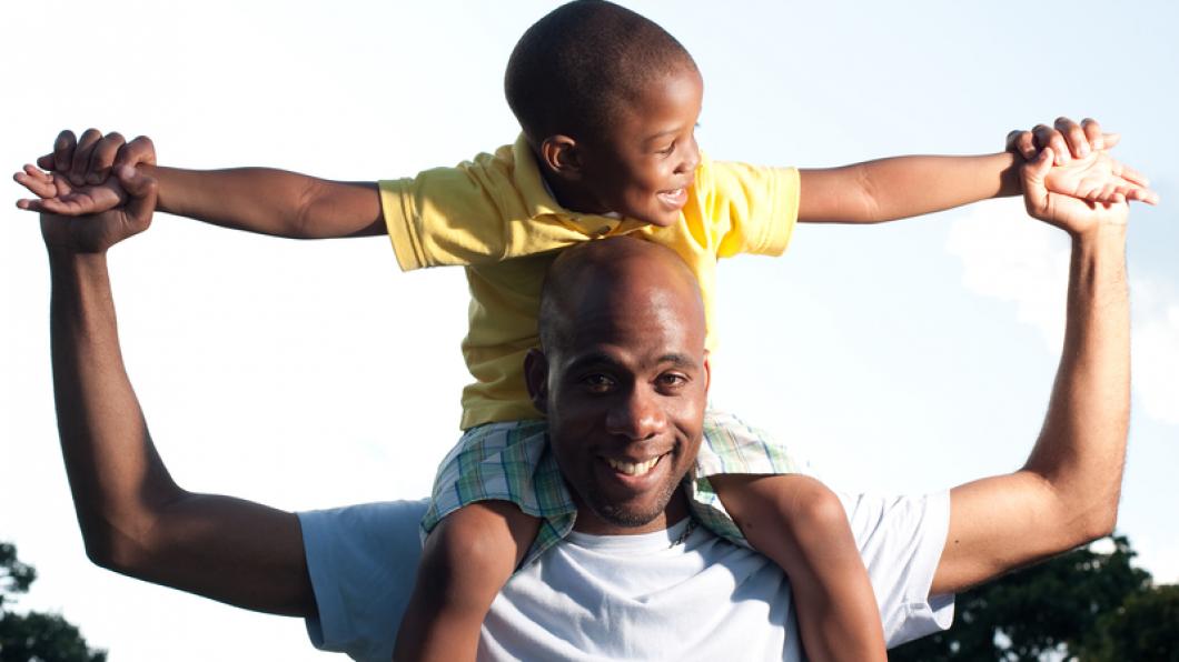 Dad holding young boy on shoulders with arms spread out