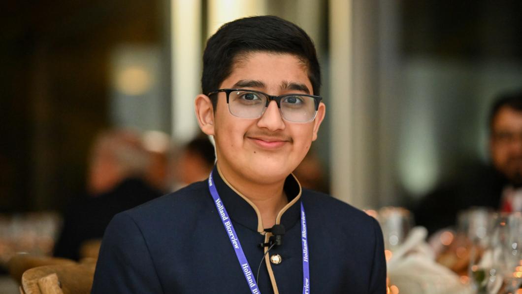 A teen with medium skin tone and short black hair wearing glasses, a blue shirt and a blue lanyard.