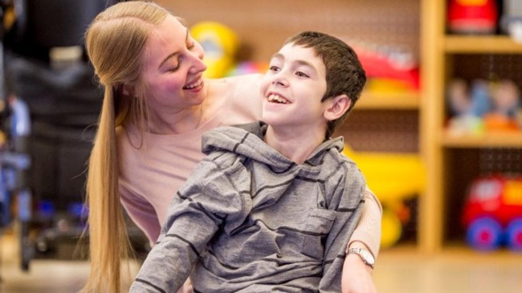 Boy with brown hair and big smile sits on floor with smiling woman with blond hair