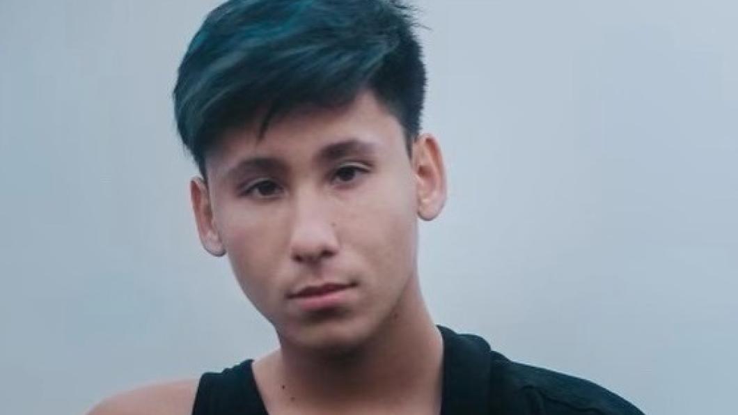 A young person with short blue hair and medium skin tone wearing a black tank top.