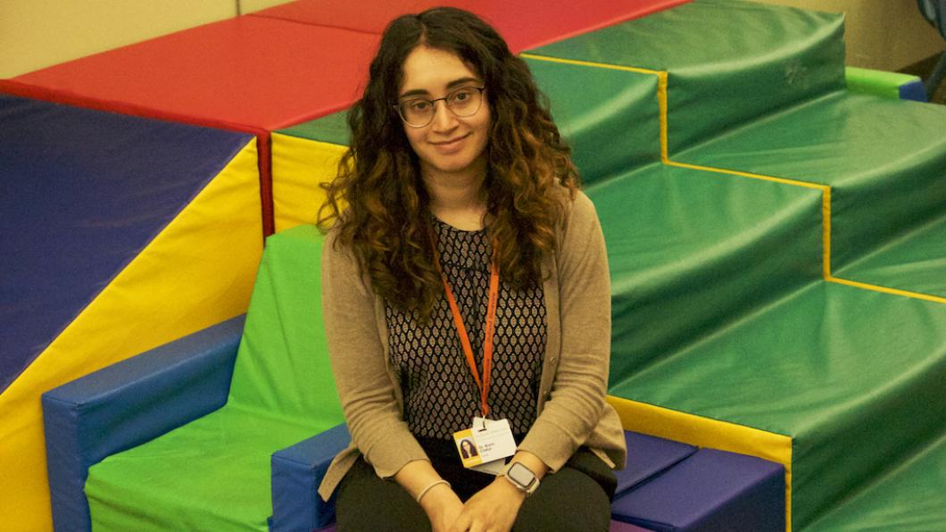 Woman with long dark wavey hair smiles sitting on colourful play structure