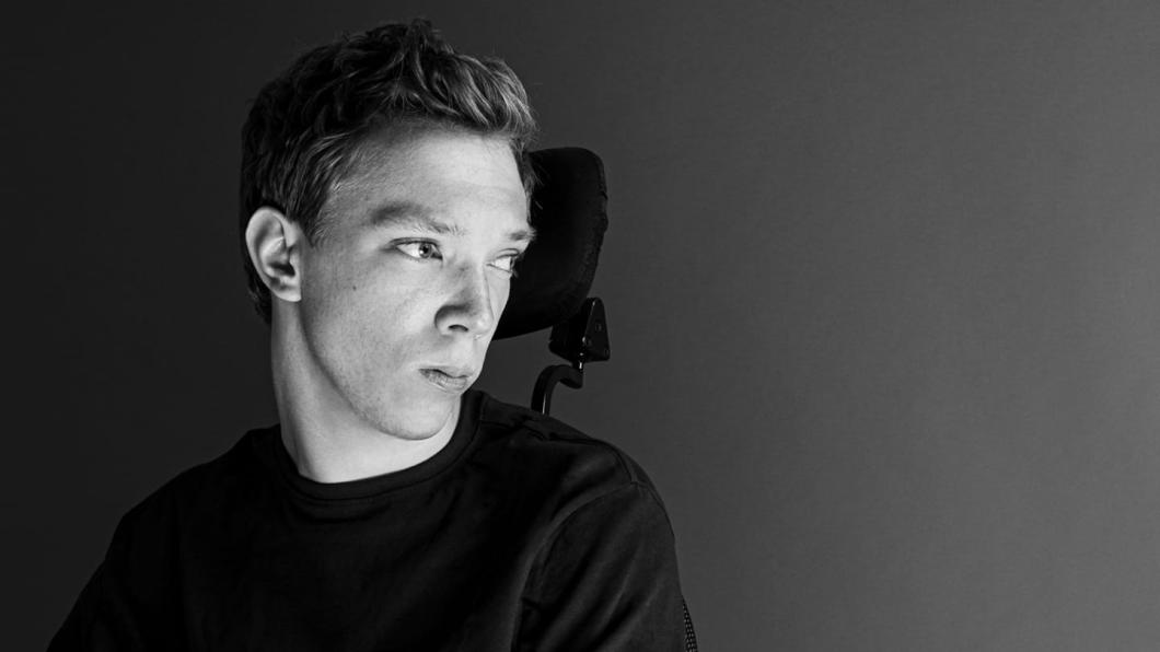 A young adult with light skin tone and short hair who uses a wheelchair.