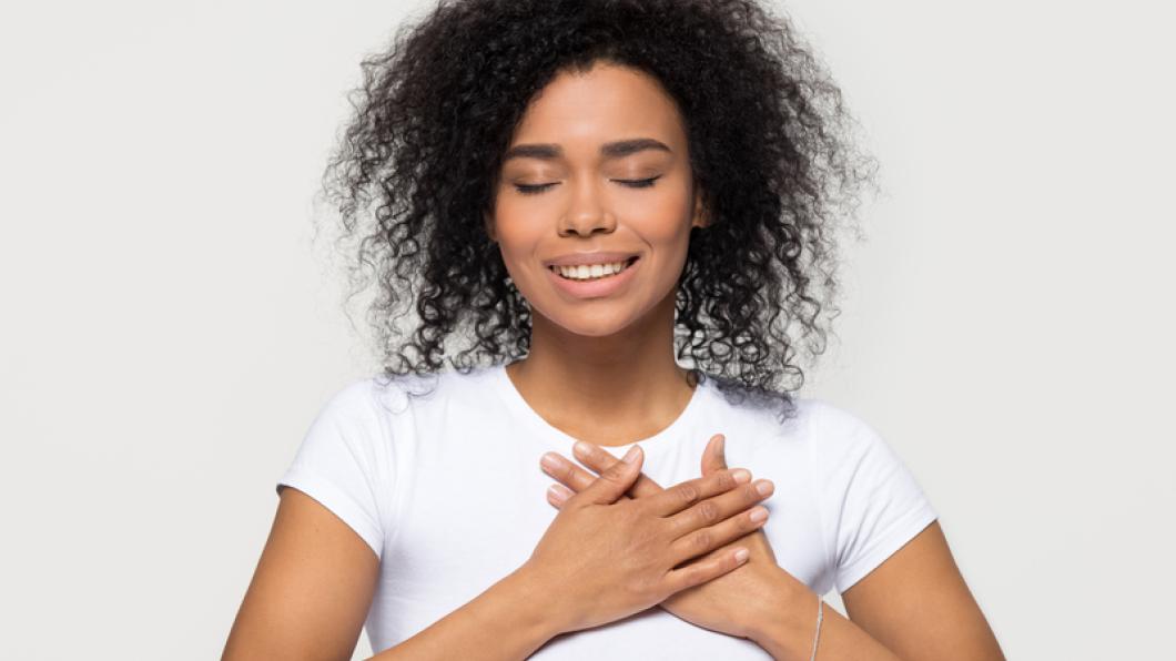 Woman with kinky hair places hands over heart and smiles