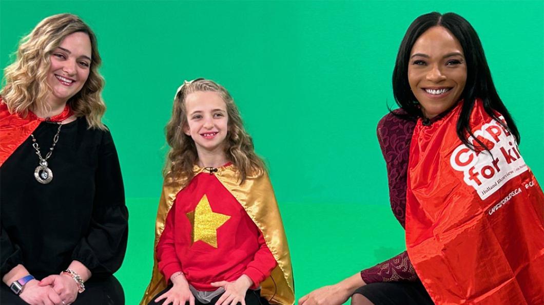 Two adults and a child with their red capes sitting in front of a green background for TV airing