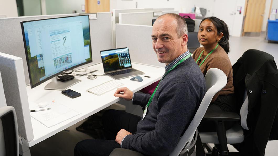 Two adults sitting in front of some computers, facing the camera