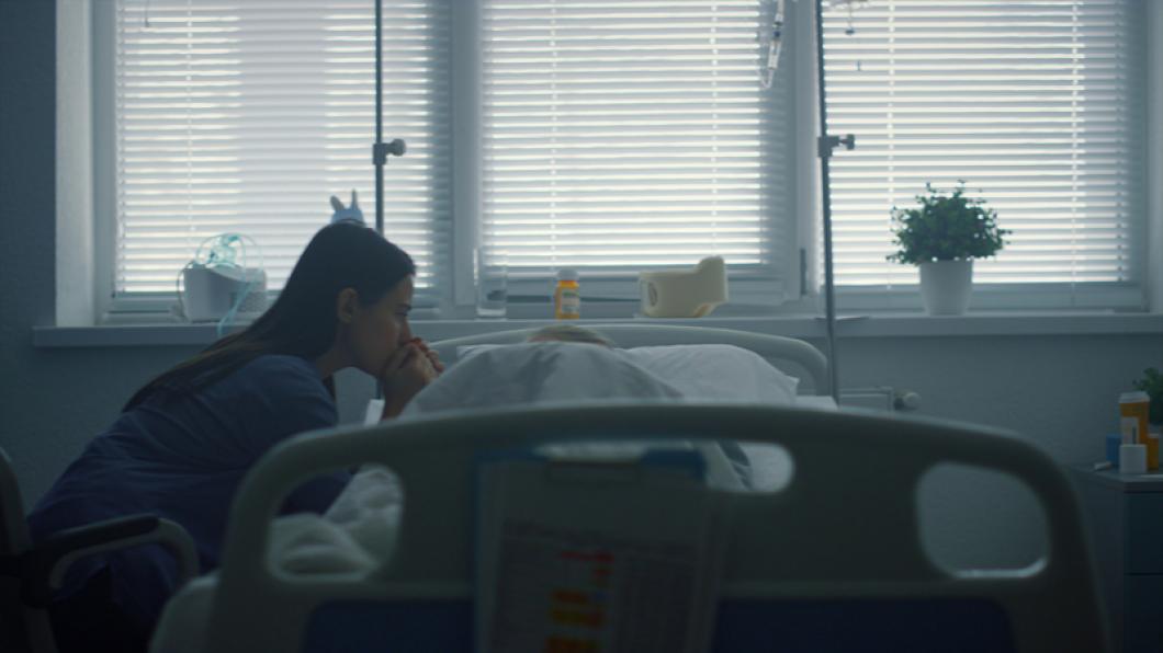 Mother with long black hair reaching over hospital bed to patient