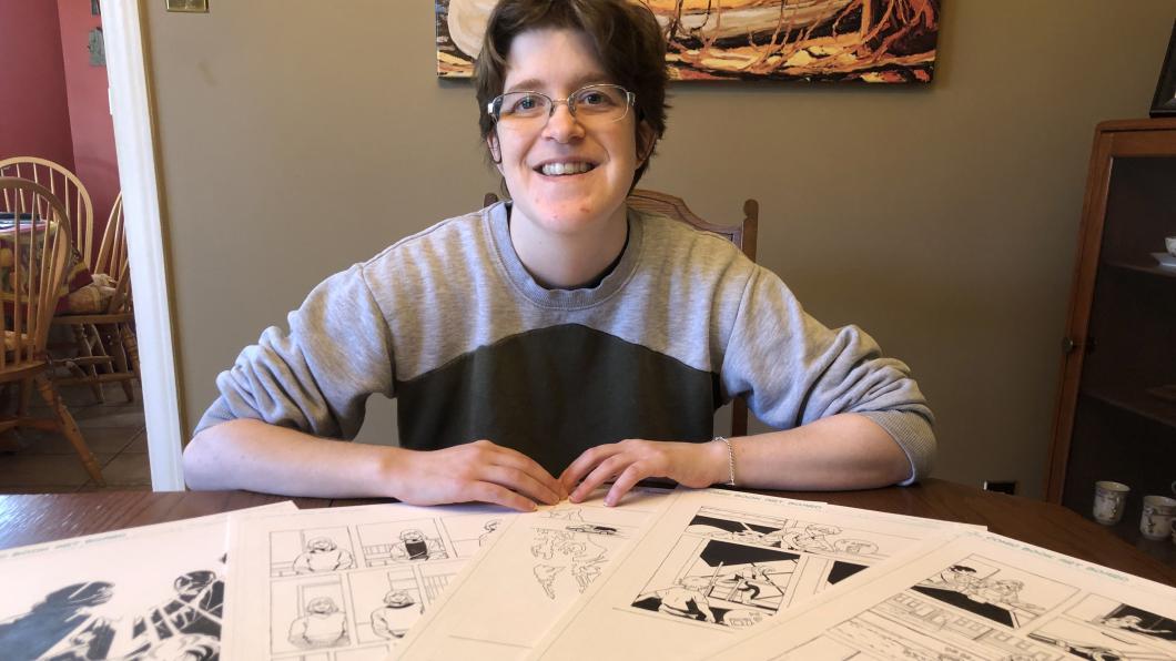 Woman sits at table where a series of comics panels are displayed