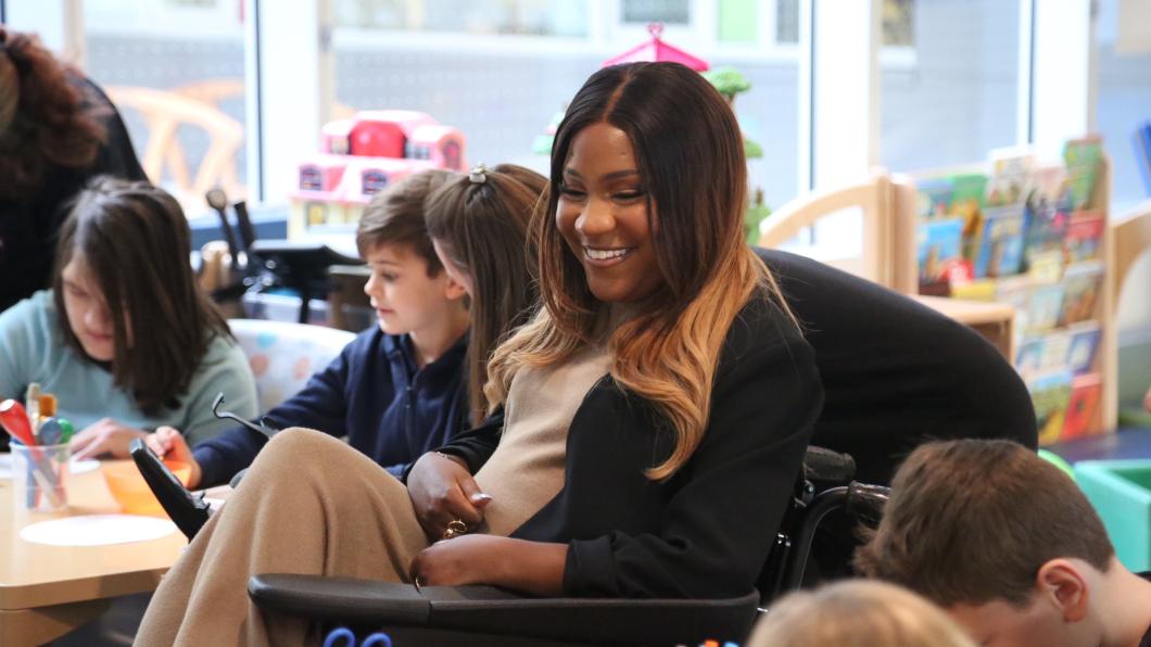 Woman in a wheelchair surrounded by students in a classroom