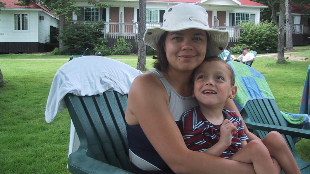 Woman with white sun hat in beach chair holding young boy