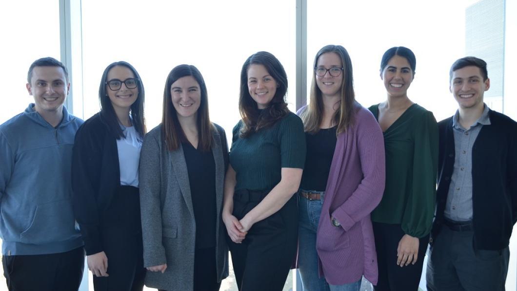 A group of researchers smile as they stand together in front of a brightly-lit window.