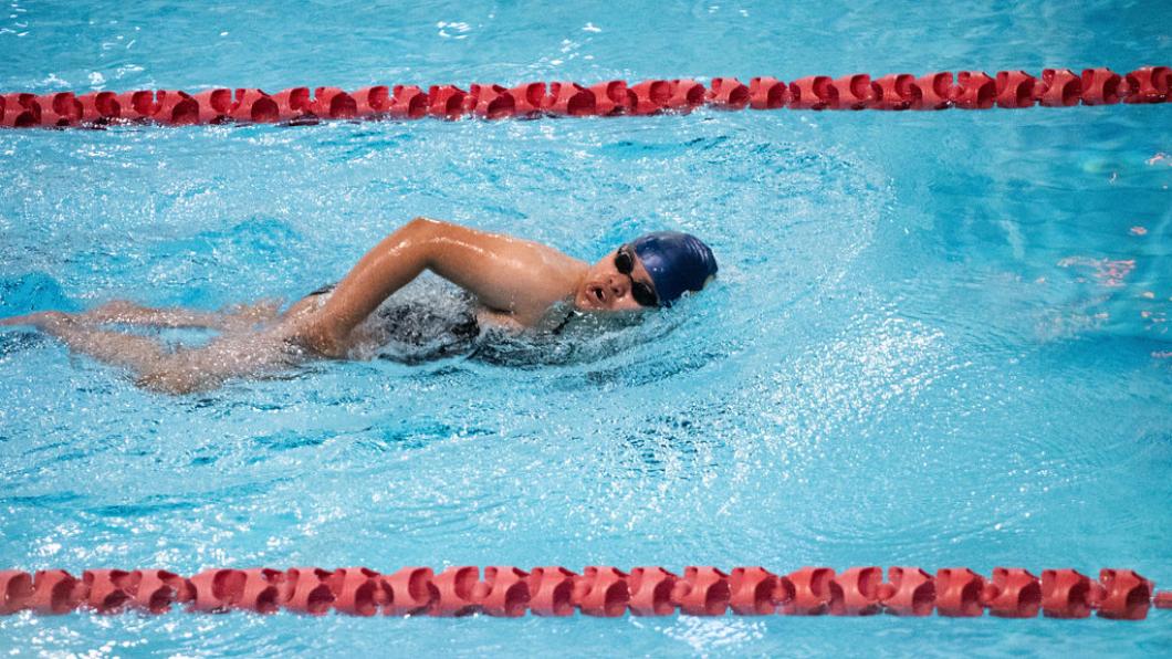 Woman in blue cap and black goggles swims the front crawl in a pool lane with red dividers