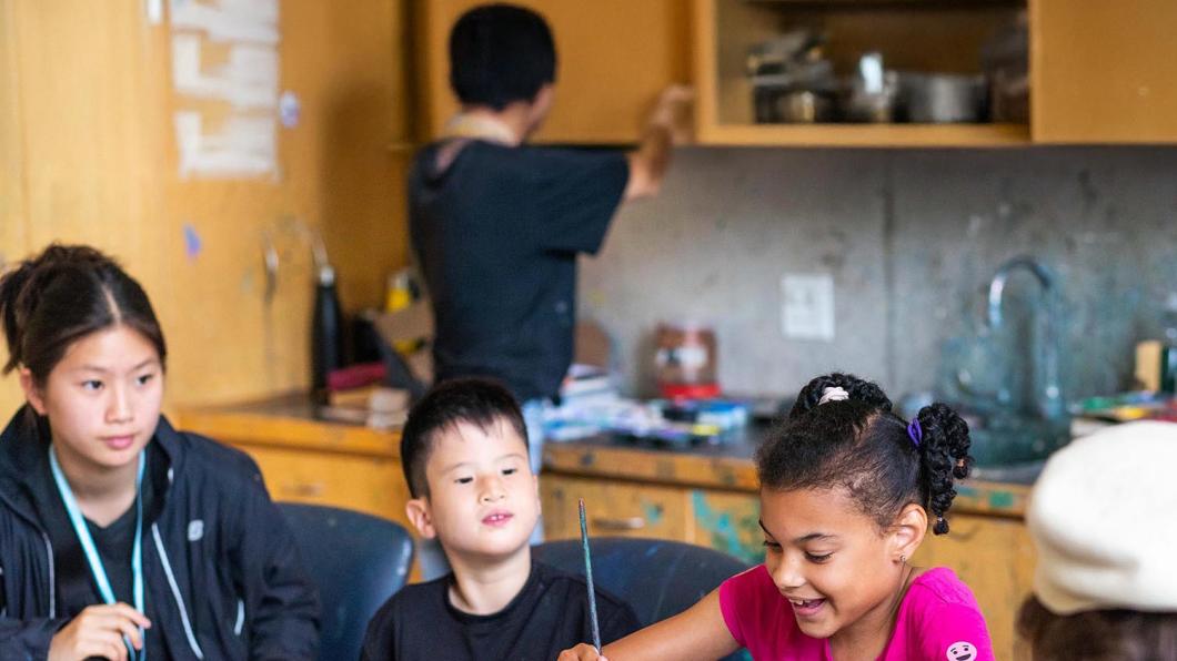 A teenager is teaching two children to draw