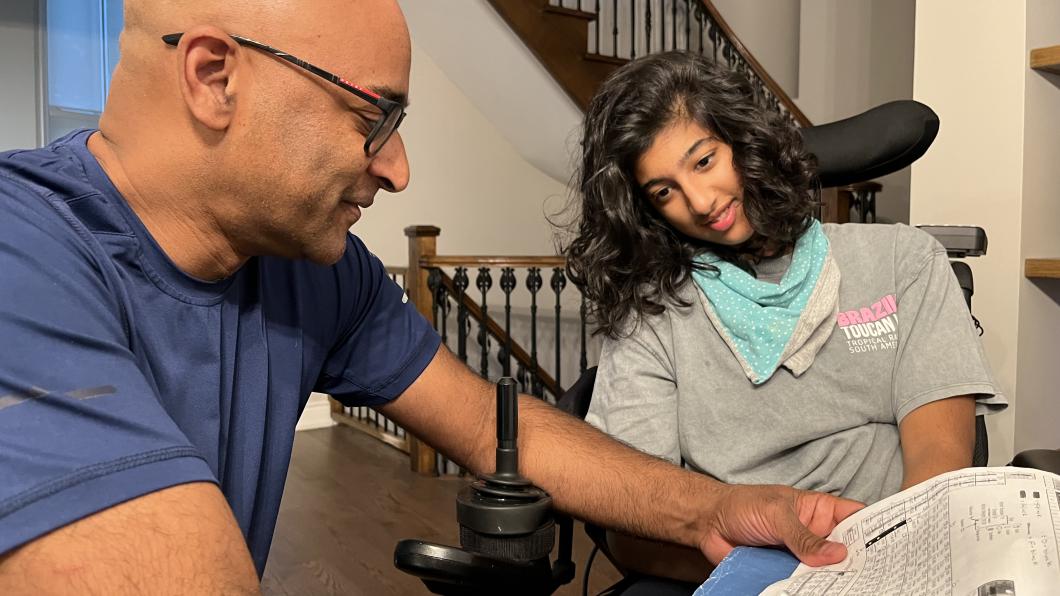 Bald man with glasses goes through a homework sheet with teen with dark hair in wheelchair