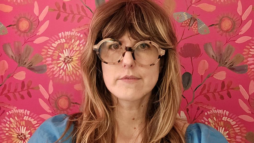 Woman with long hair and glasses against a pink wallpaper