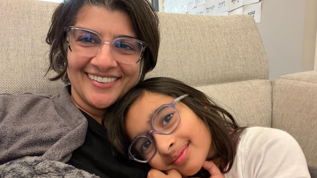 Woman with dark hair and glasses snuggles with girl with dark hair and glasses