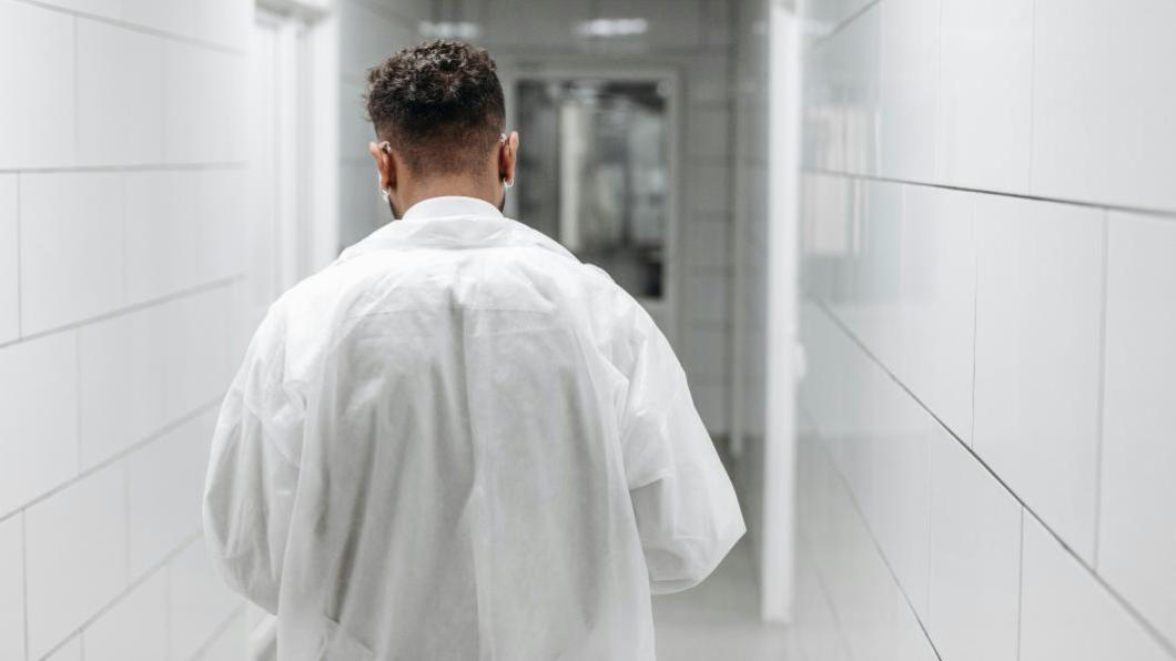Man in white doctor's coat walks down hospital hall