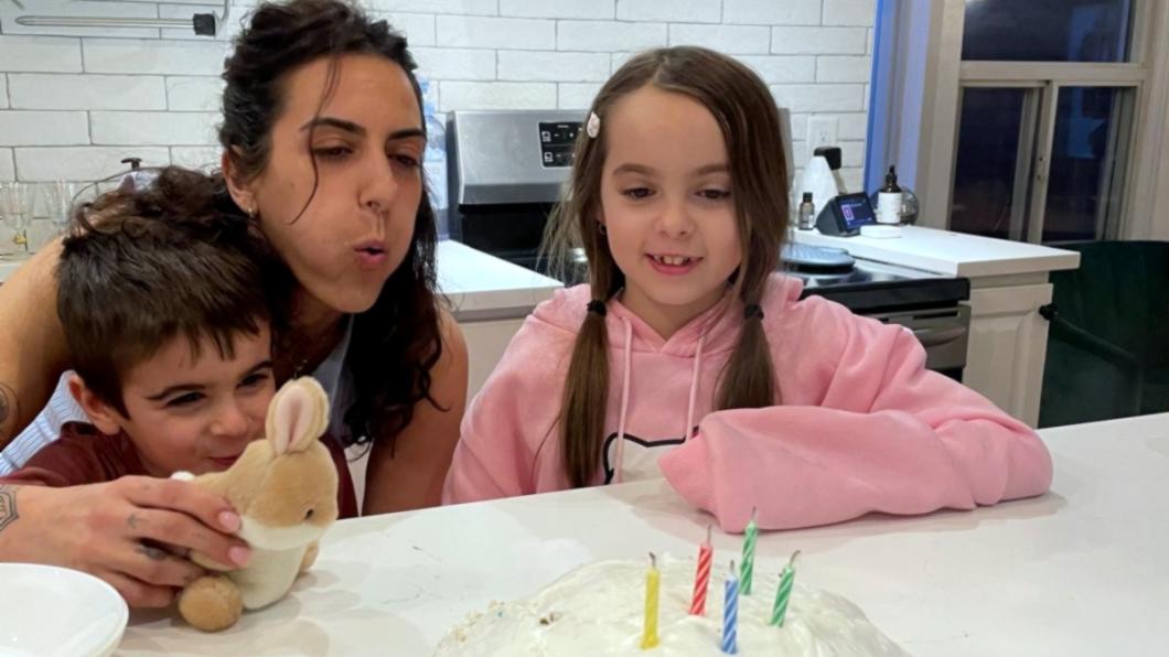 Woman inbetween a girl and boy blowing out candles on a cake