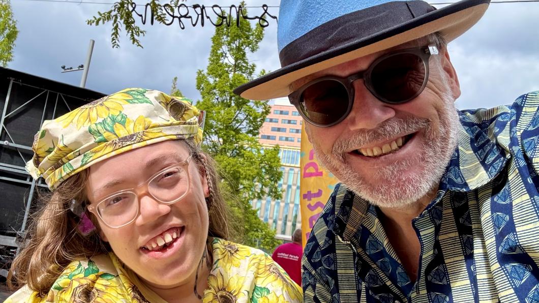 Girl with yellow sunflower hat and shirt smiles with man with blue brimmed hat and sun glasses