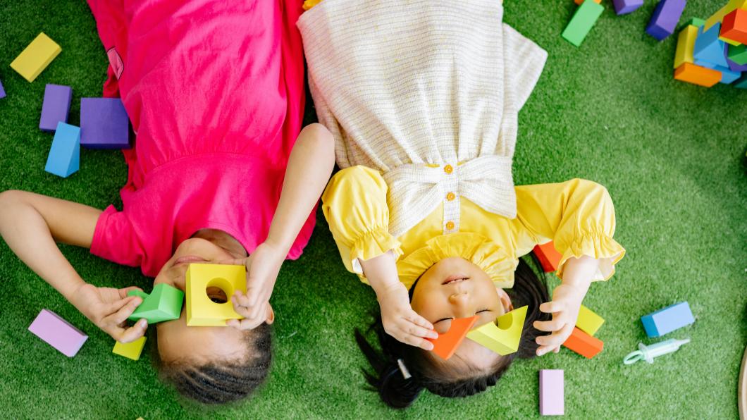 Young girls lie on floor playing with blocks
